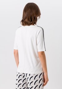 Witte T-shirt met korte mouwen, featuring zwarte schouderaccenten, een ronde halslijn en een centrale naad aan de achterkant. Zacht, getextureerd materiaal.