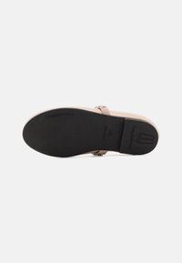 Sandal de charol nude con suela de goma negra, que presenta una sola tira y un detalle decorativo de hebilla. Diseño de plantilla cóncava.