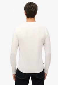 Witte T-shirt met lange mouwen, een ronde halslijn, een gladde textuur en een getailleerde pasvorm, gecombineerd met donkere jeans.