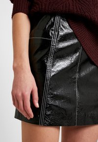 Falda de cuero sintético negra con textura brillante, detalles de costura blanca y diseño ajustado. Acompañada de un suéter de punto burdeos.