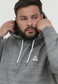 Grauer Pullover-Hoodie mit Kordelzugkapuze, strukturierter Stoff und einem kleinen weißen Dreieck-Logo auf der linken Brust.