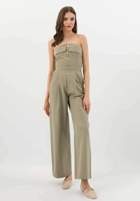 Olivově zelený overal bez ramínek s předním zipem, sklady na širokých nohavicích a přiléhavým trupem, vyrobený z hladkého materiálu.