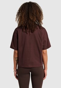 Bruine katoenen T-shirt met korte mouwen, losse pasvorm en rechte zoom. Heeft een gladde textuur en toont de achterkant van een persoon die het draagt.