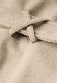 Beżowy filc z miękką teksturą, z detalem krzyżowego wyszycia na pasku. Gładki, ciepły wygląd z subtelnymi odcieniami różnicującymi.