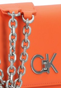 Borsa a tracolla sintetica arancione con catena argento, dotata di un accento argentato con logo. Superficie testurizzata con una finitura liscia.