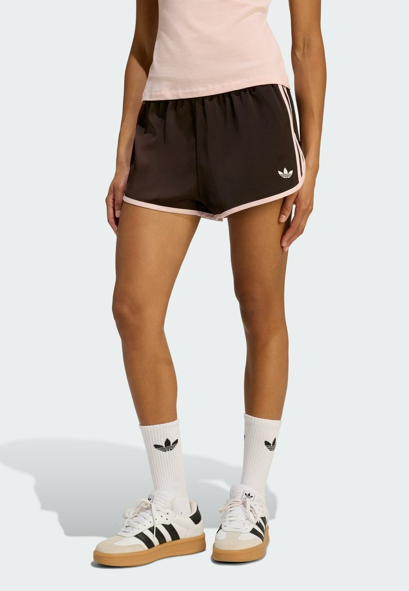 Schwarze Sportshorts mit pinkem Saum, ausgestattet mit einem elastischen Bund und einem kleinen weißen Logo auf der linken Seite. Weiße Socken und Turnschuhe vervollständigen den Look.