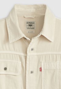 Relaxed-fit cream shirt with a button-down collar, front pockets, and silver hardware accents. Features a branded label at the neckline.