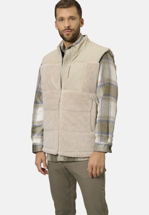 Beige fleece vest with zippered front, contrasting soft panels, and a high collar, layered over a plaid shirt in beige, blue, and white.