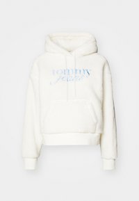 White fleece hoodie with a drawstring hood, front pocket, and ribbed cuffs. Features blue embroidered "tommy jeans" logo on the front.