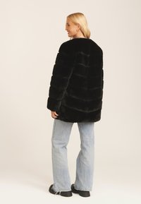 Black faux fur coat with a horizontal stripe design, oversized shape, and long sleeves, paired with light blue flared jeans and black shoes.