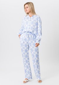 Blauwe en witte gestreepte twee-delige pyjama set. De bovenkant heeft een knoopsluiting aan de voorkant en lange mouwen; de broek heeft een elastische tailleband en een losse pasvorm.