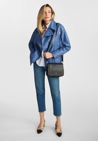 Niebieska skórzana kurtka motocyklowa, jasnoniebieska koszula zapinana na guziki, krótke dżinsy i dwukolorowe beżowo-czarne szpilki. Czarna torba na ramię.