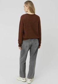 Pull en tricot marron avec des poignets côtelés et une coupe décontractée, associé à un jean en denim gris taille haute, les deux disposant de poches pratiques.