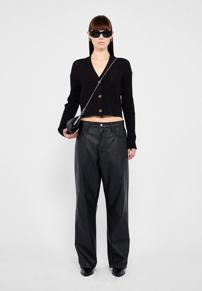 Cardigan noir court à côtes avec des boutons dorés, associé à un pantalon en cuir noir ample. Les accessoires incluent des lunettes de soleil noires et un petit sac à main.