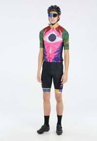 Korte mouwen fietsjersey met een multicolor abstract ontwerp in roze, groen en paars. Zwarte shorts met kleurrijke accenten. Zwarte helm en bril.