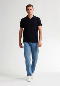 Musta lyhythihainen poolopaita, jossa etutasku yksityiskohtana, yhdistetty vaalean sinisiin farkkuihin ja valkoisiin tennareihin; sileä kangas ja klassinen malli.