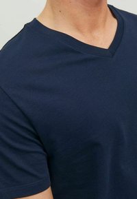 Námořnická modrá bavlněná tričko s výstřihem do V a krátkým rukávem, s hladkou texturou a prošitým výstřihem.