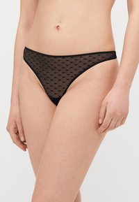 Svart genomskinlig trosa med subtilt hjärtat mönster, elastisk midjeresår och minimal täckning. Mjuk textur, lätt design.