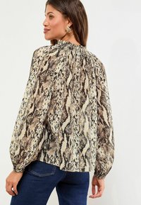 Bluza cu mâneci lungi, de nuanță bej deschis, cu un imprimeu cu șerpi negri și căprii. Prezintă un guler strâns și mâneci ample pentru un aspect lejer.