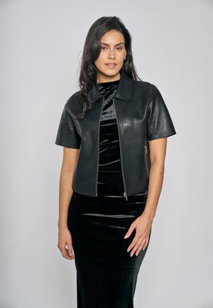 Schwarze, kurz geschnittene Lederjacke mit kurzen Ärmeln, Kragen und Frontreißverschluss; glatte Textur und taillierte Passform über einem schwarzen Samtkleid.
