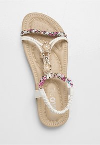 Sandalo bianco con cinturino intrecciato a motivo floreale, con gemme decorative e perle al centro. Soletta morbida color cuoio chiaro con texture traforata.