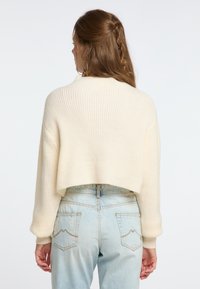 Pulover scurt din lână cu dungi, cu o croială lejeră și mâneci lungi, asortat cu blugi cu talie înaltă de culoare albastră deschisă, evidențiați prin cusături decorative.
