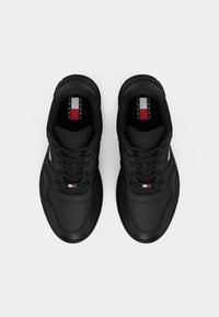 Baskets noires avec une texture lisse, présentant un design à lacets, une pointe perforée et un accent de logo en rouge, blanc et bleu sur la languette.