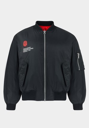 Czarna bomberka z czerwonym wnętrzem, zamek błyskawiczny, ściągacze przy mankietach oraz haftowane logo z przodu i na rękawie. Zawiera boczne kieszenie.