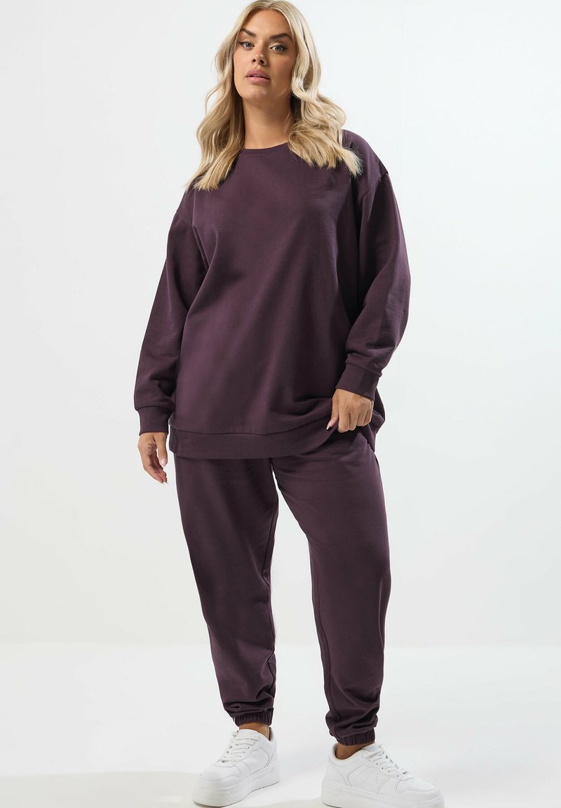 Lila Sweatshirt und passende Jogginghose aus weichem Stoff. Das Sweatshirt hat eine lässige Passform, Rundhalsausschnitt und lange Ärmel. Weiße Sneakers runden den Look ab.