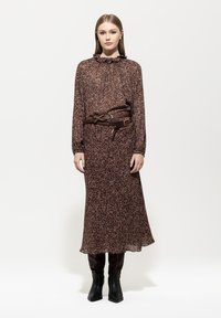 Braun gemustertes Midi-Kleid mit rüschendem Ausschnitt, tailliert mit einem braunen Gürtel. Getragen mit kniehohen schwarzen Lederstiefeln. Glatter Stoff, lockere Passform.