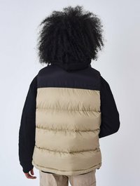 Gilet imbottito con parte inferiore beige e parte superiore nera. Presenta un cappuccio e maniche nere texturizzate, progettato per isolamento e comfort.