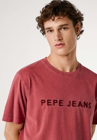 Camiseta de algodón granate con mangas cortas, cuello redondo y "PEPE JEANS" bordado en un tono más oscuro en el frente.