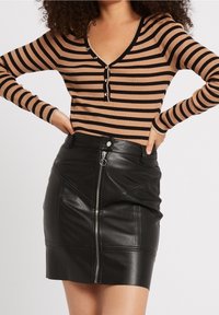 Haut à manches longues rayé et côtelé marron et noir avec col en V et fermeture à boutons, associé à une mini-jupe en cuir noire avec une fermeture éclair frontale.