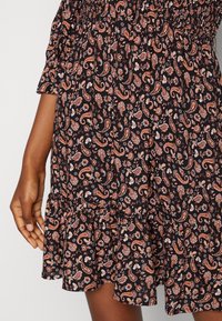 Černé šaty s paisley a květinovými vzory v oranžové a bílé. Volánkový lem a elastický korzet. Měkká látka; dlouhé rukávy.