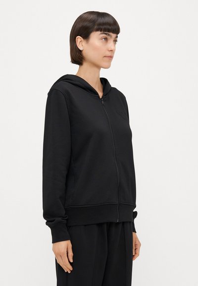 Črna zip-up kapuca iz mehkega blaga, ki ima kapuco, rebraste manšete in subtilno logotip na prsih. Preprost, brez okraskov oblikovanje.