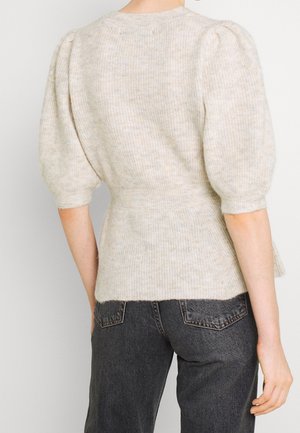Femme portant un pull beige clair à manches bouffantes et un jean taille haute gris foncé, vue de dos.