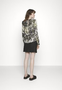 Blusa de manga longa com um padrão abstrato em verde, preto e branco; combinada com uma saia mini preta texturizada e sandálias de plataforma pretas.