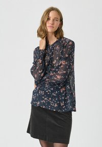 Bluză bleumarin cu imprimeu floral, mâneci lungi transparente și închidere cu nasturi. Asortată cu o fustă neagră, cu detalii din țesătură texturată vizibile.