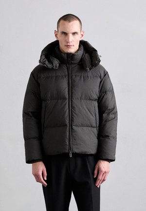 Giubbotto imbottito nero con superficie texturizzata, dotato di colletto alto, chiusura con zip e cappuccio ampio. Realizzato in materiale isolante.