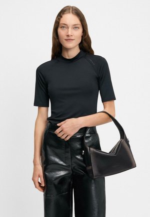 Czarna krótka bluzka z wysokim kołnierzem, zestawiona z błyszczącymi czarnymi skórzanymi spodniami i usztywnioną czarną torebką.