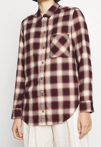 Rote und beige karierte Flanellhemden mit langen Ärmeln, einer Knopfleiste und einer Brusttasche. Sanfte Textur und abgerundeter Saum.