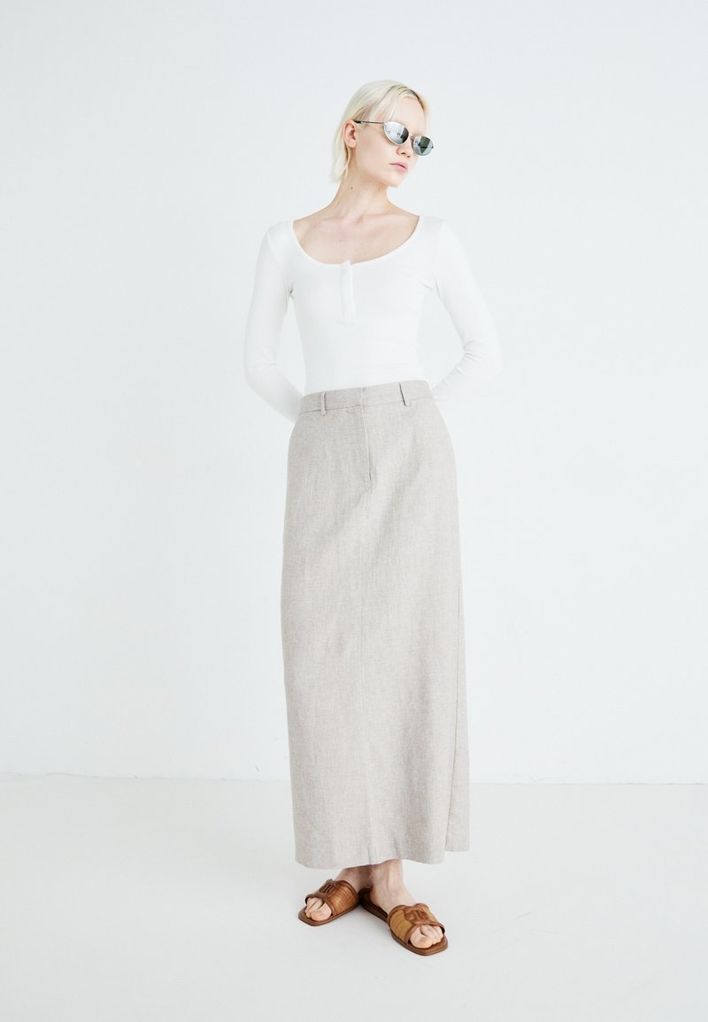 Lange, lichtbeige linnen rok met een rechte silhouet, gecombineerd met een fitted witte blouse met lange mouwen en brown slide sandalen.