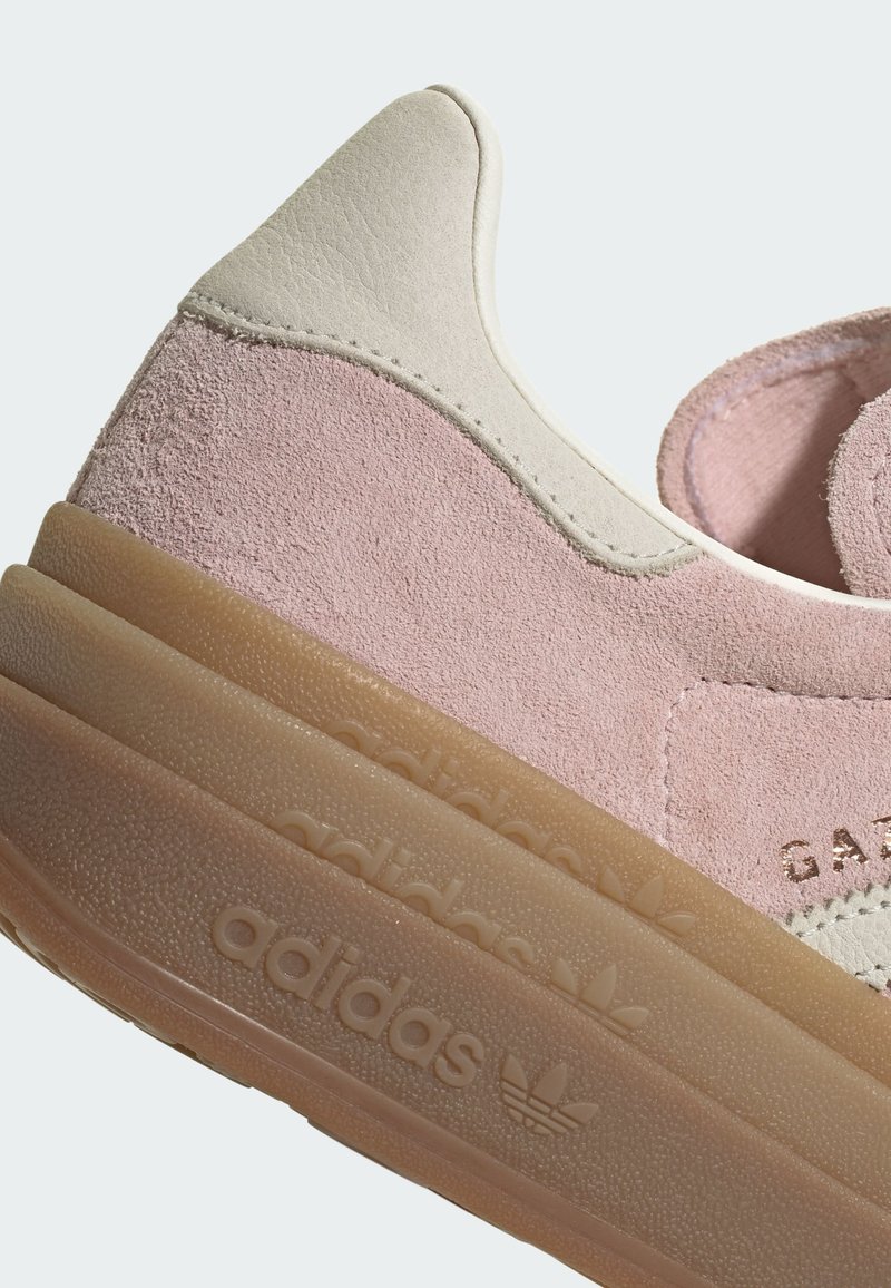 Roze suède sneaker met een beige leren hiel, een gestructureerde tussenzool en geperste logodetails. Afgeronde vorm en minimalistisch ontwerp.
