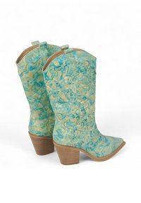 Botas de vaquero turquesa con un diseño grabado en floral, puntas afiladas y un tacón de madera apilada, hechas de cuero texturizado.