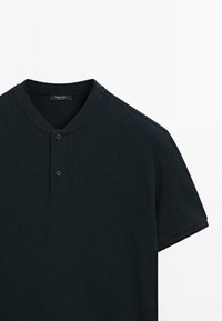 Mørkegrøn kortærmet polo skjorte lavet af ribbet stof. Har en knaplukning ved halsen og kontrastkant på ærmerne.