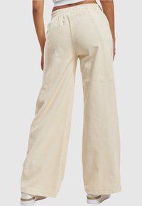 Weite Cordhose aus Baumwollcord in hellem Beige, mit strukturiertem Rippenmuster, elastischem Bund und sauberen Säumen, von hinten gezeigt.