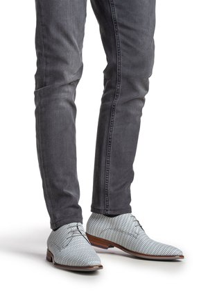 Chaussures à motifs gris avec une texture lisse, bout rond et semelles en cuir marron, associées à un jean foncé ajusté.
