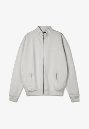 Sweat-shirt zippé gris clair avec un col montant, deux poches latérales zippées et des poignets côtelés. Texture lisse avec un minimalisme en matière de branding.