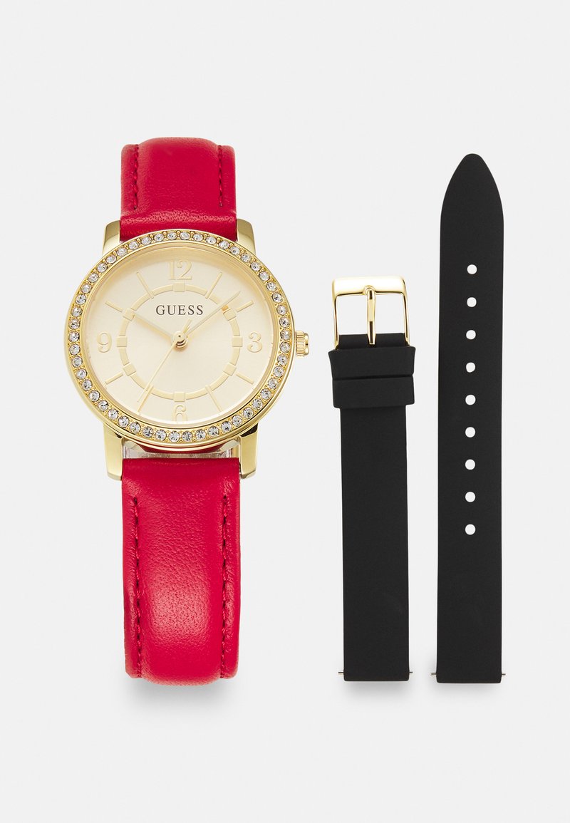 Reloj de oro con una esfera beige, acentos de cristal, correa de cuero rojo y una correa adicional de goma negra con agujeros de ajuste.