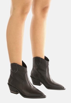 Mustat nahkaiset nilkkurit, joissa on terävä kärki, kulmikas muotoilu ja keskipitkä lohkokorko, koristeltu aaltoilevilla ompeleilla.